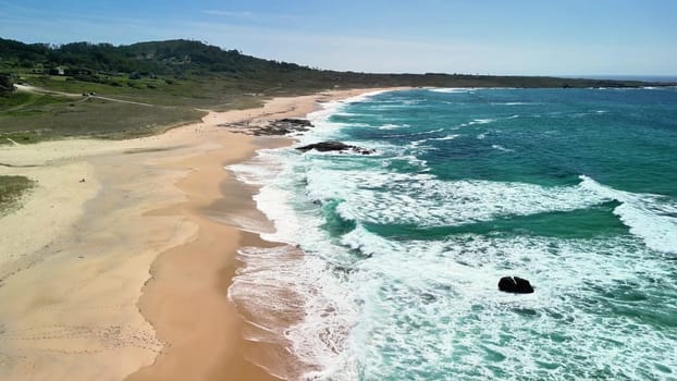 Enjoy a breathtaking aerial view of a tranquil beach with gentle waves and lush green hills surrounding it