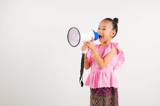 Portrait Thailand kid girl smiling traditional Thai dress costume shouting by megaphone, studio shot isolated white background, kindergarten screeching through in megaphone announces discounts