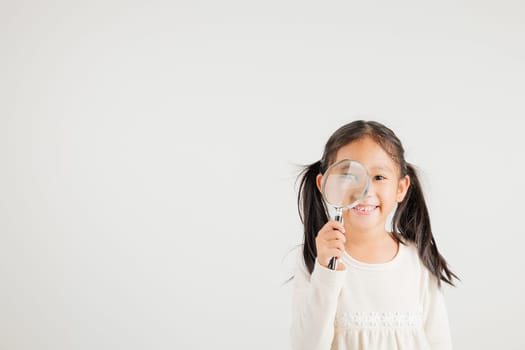 Asian little kid girl funny looking through magnifying glass at studio shot isolated on white background, Happy kindergarten child lifestyle smiling exploring holding magnifier searching, Education