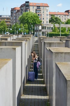 Berlin, Germany – May 01, 2025: Female tourist with suitcase between the concrete blocks at the Holocaust memorial in downtown Berlin