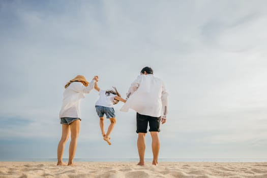 An Asian family bursts with excitement father and mother holding children joyfully jumping into air on beach. beautiful ocean forms picturesque background capturing moment of family happiness.