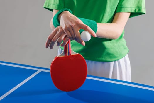 Table tennis player in green preparing to serve, holding ping pong paddle and ball on blue game table.