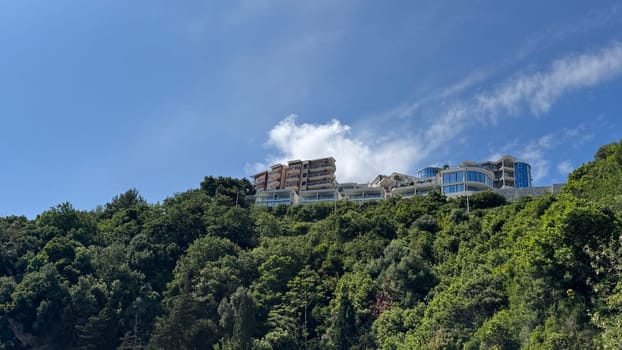 Budva, Montenegro - May 18, 2025: Luxury apartments perched on hillside amidst vibrant green trees and clear blue sky