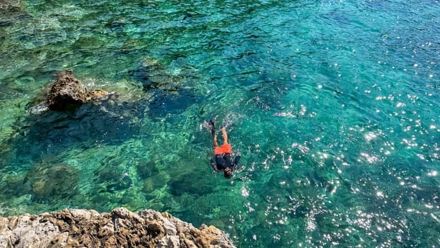 Budva, Montenegro - May 18, 2025: Male swimmer enjoys clear turquoise water near rocky shoreline with sunlight