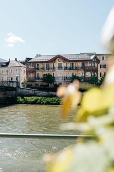 A vibrant building stands along the riverbank in Bad Ischl under a clear blue sky. Lush greenery frames the scene, highlighting the charm of this picturesque location.