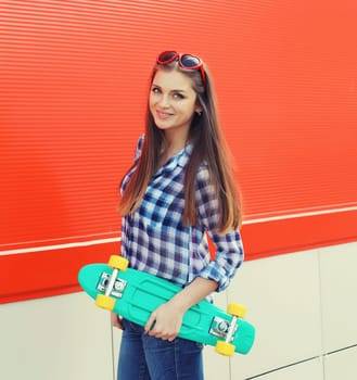 Summer portrait of happy cheerful stylish young woman with skateboard, teenager girl in casual clothes, glasses posing on red background on city street