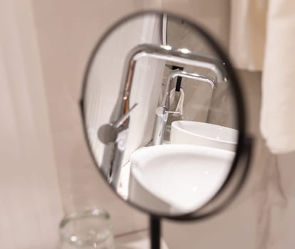 A round bathroom mirror reflecting faucet and sink in a clean stylish washroom.