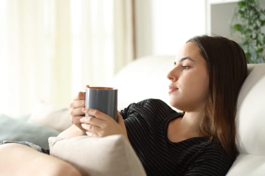 Abstracted woman drinking coffee looking away sitting on a couch at home