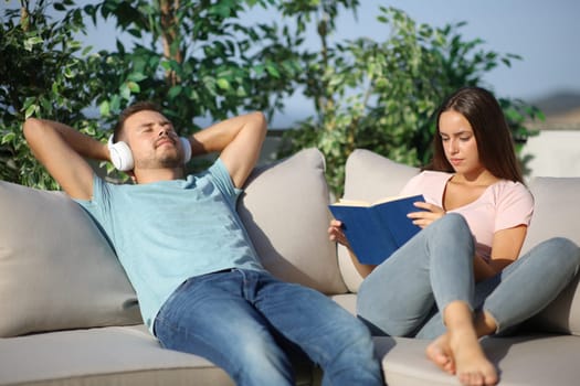 Couple relaxing spending time in different ways reading book and listening music in a terrace