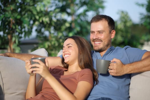 Happy couple sitting in a sofa in the garden drinking coffee at home