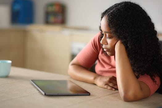 Serious black woman watching media on tablet in the kitchen at home