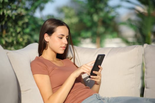 Serius woman using mobile phone sitting in a garden at home