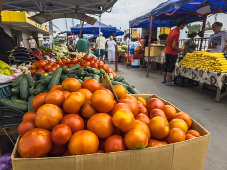Bustling vegetable street market, Various fresh produce displayed under blue canopies with people shopping on a cloudy day. in Sokuluk, Kyrgyzstan - June 28, 2024