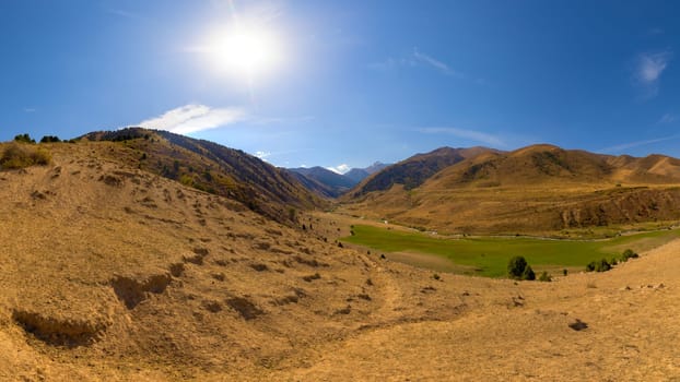 dry dust covered hill in mountains with blue sky and sun above at autumn day in Kyrgyzstan
