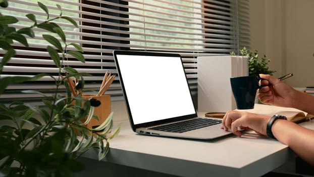Close up of hands on laptop with blank screen at desk surrounded by plants in a cozy home office.