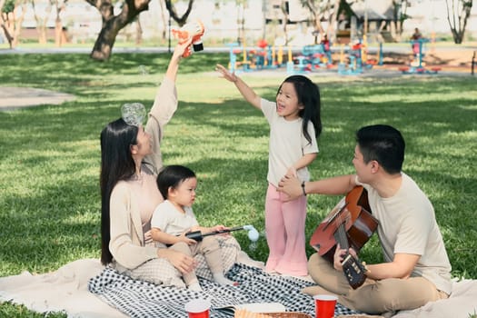 Happy family playing with bubbles during a picnic in the park.
