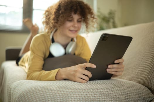 Female using digital tablet while lying comfortably on a sofa.