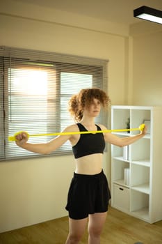 Focused woman in athletic wear using resistance band for upper body at home.