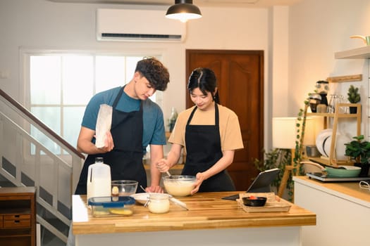 Cheerful young couple preparing pancake batter together in kitchen.