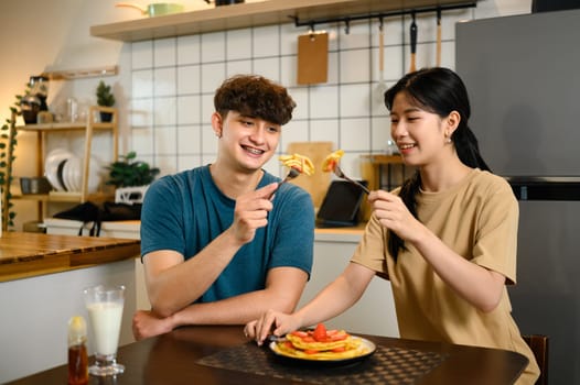 Romantic couple enjoying pancake breakfast together in a cozy kitchen.