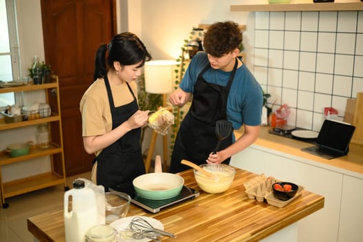 Happy couple preparing homemade pancakes in a warm kitchen.