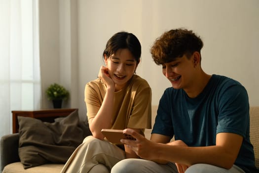 Couple enjoys browsing a smartphone together on sofa in their living space.