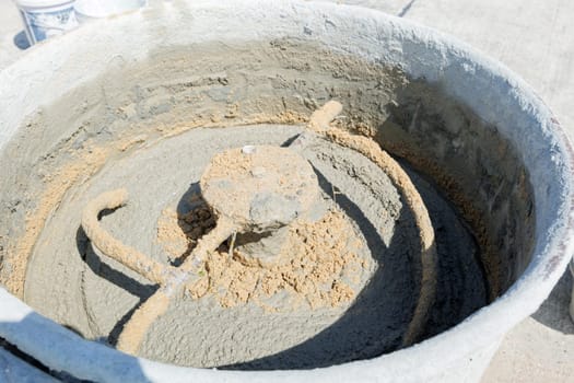 Mixer blades visible churning gray mortar and sand inside, highlighting the concrete preparation process for building projects.
