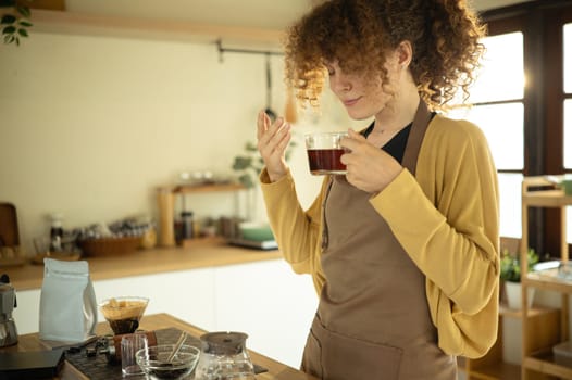 Relaxed young woman smells her freshly brewed coffee in a warm and inviting kitchen.