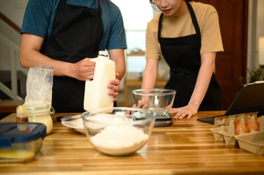 Cheerful young couple preparing pancake batter together in kitchen.