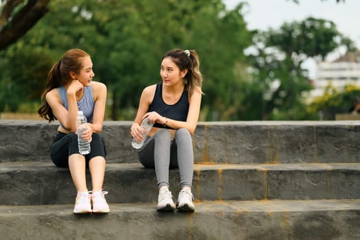 Sporty women take a break on concrete steps with water bottles in hand.