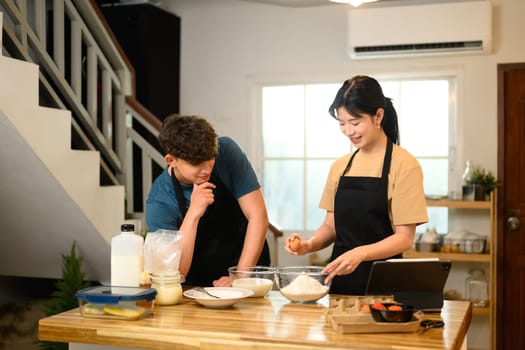 Cheerful young couple preparing pancake batter together in kitchen.