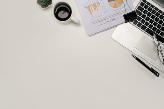 Top view of modern office desk with financial report, laptop, coffee cup, and glasses.