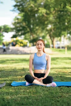 Woman practicing meditation and deep breathing on a yoga mat in a natural environment.