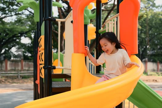 Cheerful little girl sliding at colorful playground.