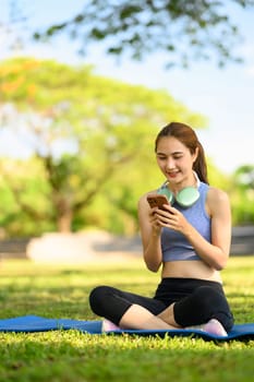Sporty young woman uses her phone during a break in the park.
