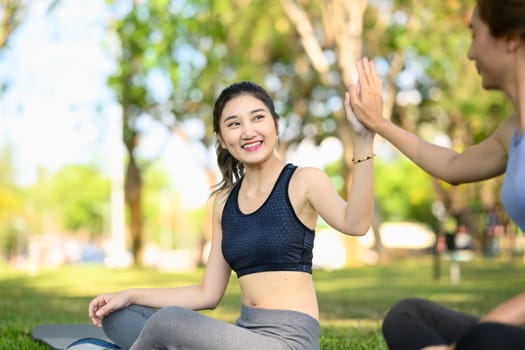 Two athletic women share a cheerful high-five after completing an outdoor workout in a green park..
