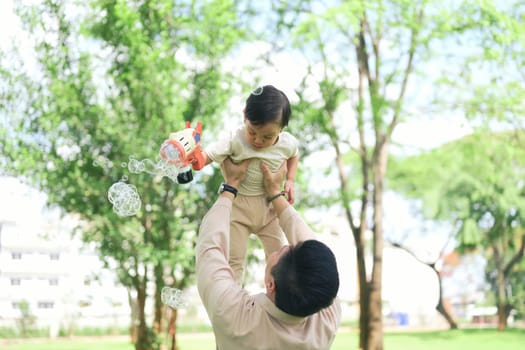 joyful dad lifts his toddler high in the air as the child holds a bubble gun.