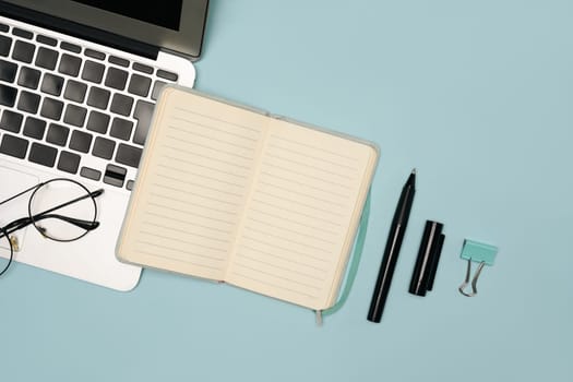 Flat lay image showing laptop, lined notebook, and office supplies on a blue background.