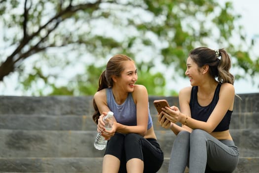 Sporty women relax on stone steps, sharing a joyful moment after a workout.