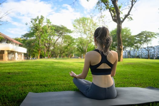 Woman practicing meditation and deep breathing on a yoga mat in a natural environment.