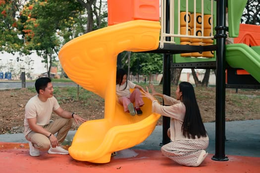 Joyful little girl enjoys sliding with support from her loving parents on both sides.
