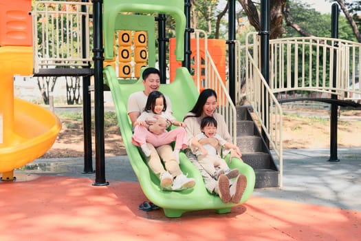 Parents and children enjoy a fun moment riding down a double slide, laughing during a sunny day.