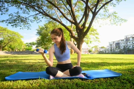 Female fitness enthusiast lifting a dumbbell on mat in a tranquil urban park.