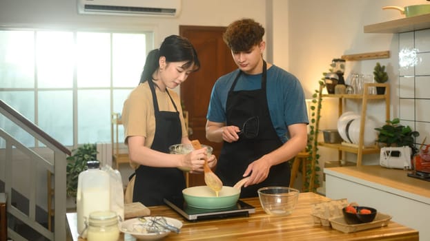 Happy couple wearing aprons preparing breakfast in modern kitchen.