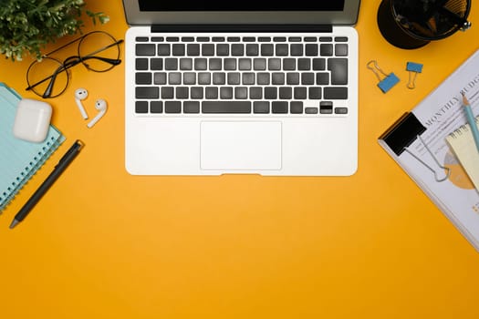 Flat lay of modern workspace with laptop, stationery and documents on yellow background.