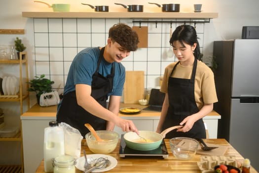 Happy couple wearing aprons preparing breakfast in modern kitchen.