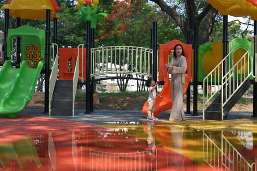 Mother and toddler exploring colorful playground after rain.
