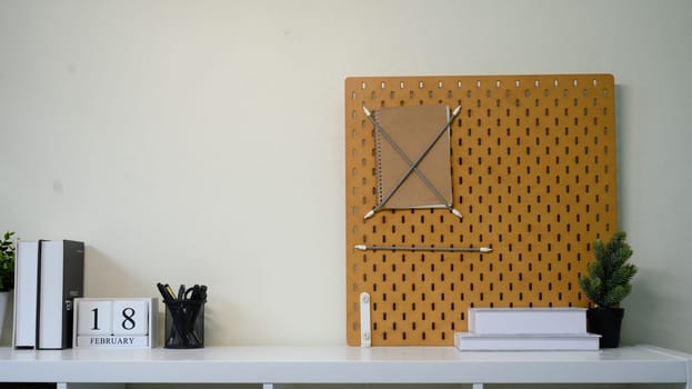 Minimalist home office shelf with pegboard, books, stationery, and indoor plants.