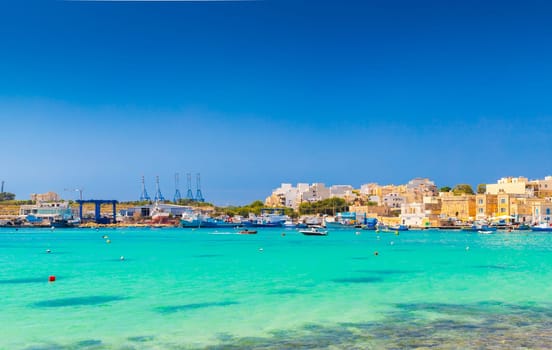 Beautiful cityscape of Marsaxlokk, a small coastal town in Malta, with turquoise clear sea water in the foreground.
