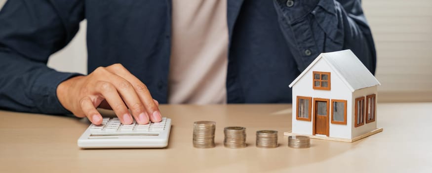 Calculator and house model on a desk with coins stacked. Represents tax savings, property value increase, and real estate profit planning for cash flow and smart investment decisions.